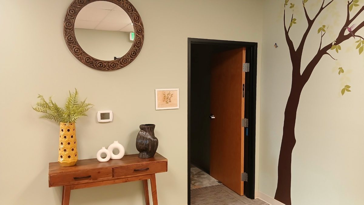 Hallway with a round carved mirror, wooden table, fern and a painted tree